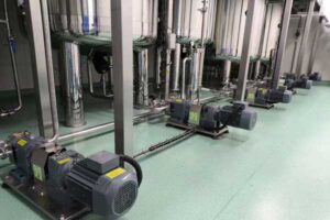 row of industrial pumps installed on a clean, green floor, connected to stainless steel pipes in a modern facility